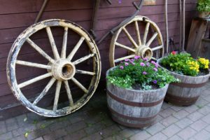 esempio di riciclo creativo nell'arredamento di esterni - vasi di fiori da vecchie botti di legno con ruote sullo sfondo come oggetti decorativi