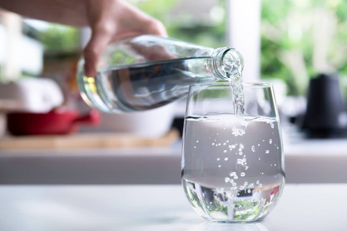 una mano versa acqua in un bicchiere su un tavolo acqua naturale senza bollicine
