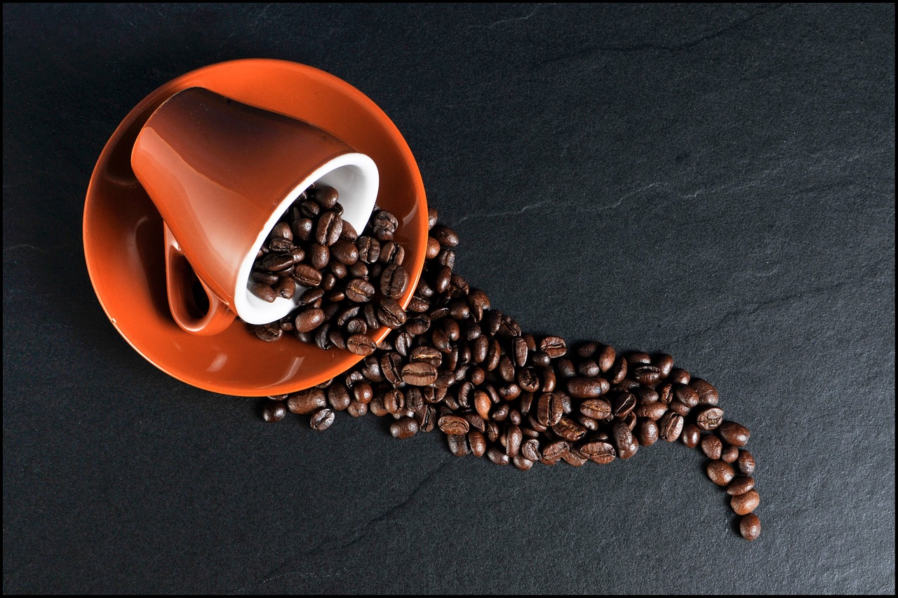 tazzina da caffè arancione su piattino da cui fuoriescono chicchi di caffè vista da alto tazzina da caffè arancione su piattino da cui fuoriescono chicchi di caffè vista da alto