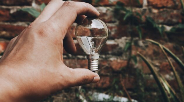 una mano che tiene una lampadina davanti ad un muro