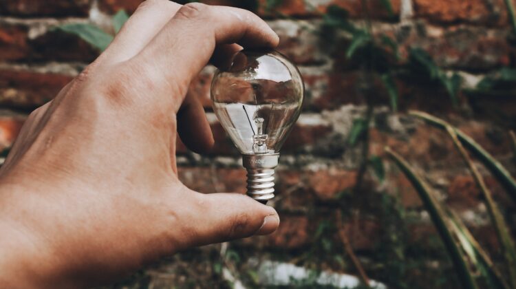 una mano che tiene una lampadina davanti ad un muro